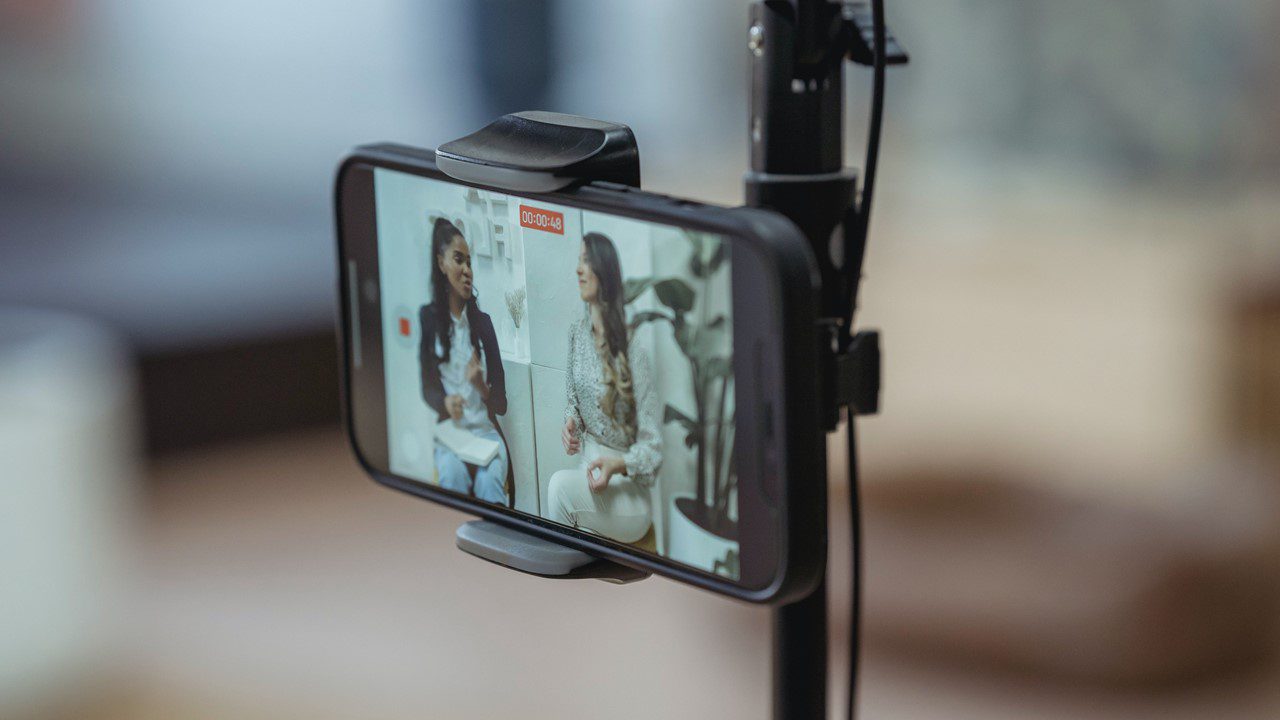 Influencer Marketing shown through the back of a smartphone on a tripod as it is capturing video of two women talking to camera.